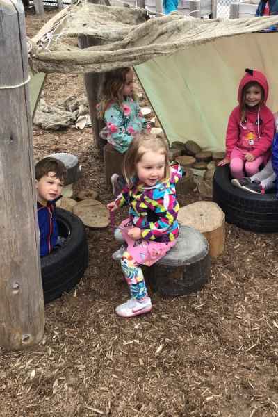 preschoolers sitting under a tarp on logs